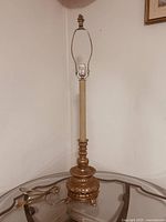 Full view of the vintage table lamp showing the tall cream body and gold ornate base with electrical cord visible, no lampshade attached.