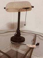 Photo of vintage table lamp with textured glass shade and pull chain on a glass table.