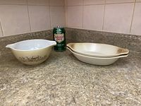 Photo showing the Pyrex mixing bowl with Forest Fancies mushroom design next to two Sunmarc stoneware baking dishes with a can for scale, on countertop.