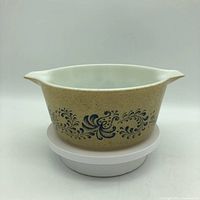 Front and side view of vintage Pyrex Homestead print serving dish showing its beige speckled design with blue floral pattern and dual spouts.