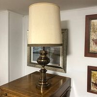 Straightforward photo of the vintage solid brass lamp sitting on a wooden surface. Shows the full lamp and shade with clear view of the brass base details and fabric shade texture.