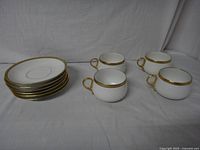 Four cups and six saucers displayed with white background, showing gold trim on rims and handles.