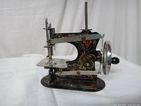 Side view of the Casige toy sewing machine showing gold scroll design and hand crank wheel.