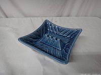 Front-side angled view of the blue ceramic square ashtray showing the textured leaf design and the cigarette rests.