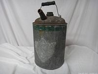 Front and side view of the galvanized kerosene can showing aged metal surface, spout, and handle with green wooden grip.