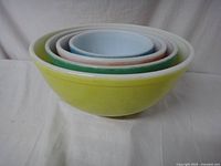 Four vintage Pyrex mixing bowls nested inside each other showing graduated sizes and colors (yellow, green, pink, blue). Color fading visible.