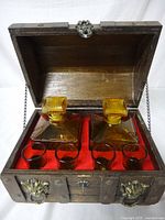 Wooden treasure chest open showing interior with 2 amber glass decanters and 4 matching shot glasses inside red felt lining.