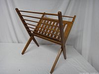 Side angle view of the folding wooden magazine rack showing slatted design and crossed legs