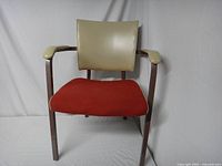 Front view of the mid-century modern industrial chair showing red fabric seat, beige vinyl backrest and armrests, and brown metal frame.