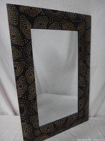 Front angled view of rectangular wall mirror showing Native Australian inspired dot pattern on black frame and clear mirror surface.