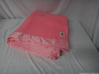 Folded pink wool blanket showing satin edging and label patch.