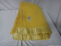 Folded yellow wool blanket with satin ruffle edging neatly displayed on white surface