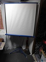 Front view of vintage Focal projector screen fully extended on tripod stand, showing white screen surface with blue edging.