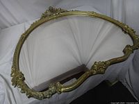 View of the full ornate oval mirror frame showing detailed gilded scrolling and floral design without glass