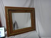 Front view of the vintage rectangular mirror showing the wood frame with gold-tone floral embossed inner frame and reflective glass.