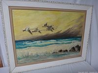 Full view of framed painting showing group of flying swans over ocean waves with yellow sky