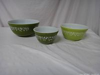 Three Pyrex mixing bowls of different sizes and shades of green with white interior and white floral Spring Blossom pattern on the exterior.