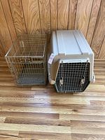 Two animal crates side by side on a wooden floor, one metal wire crate, one plastic kennel crate.