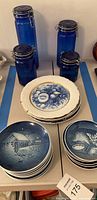 Blue glass jars and ceramic plates stacked on a table with blue painter's tape underneath