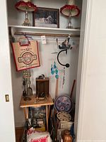 Closet shelf with two vintage-style table lamps, framed art, tote bag hanging, wind chimes, decorative items including wall clock and trays.