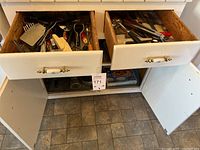 Wide view of two open kitchen drawers showing multiple kitchen utensils and tools inside, plus lower cabinet doors below the drawers.