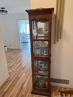 Full view of the wooden curio cabinet standing on hardwood floor in a hallway area.