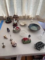Overview of all collectibles and decor items on a table under window light. Includes figurines, glass dishes, metal bells, and a ceramic bowl.