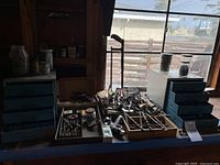 Wide view of assorted tools, drill bits, screws, and hand tools arranged on table and in drawers in a wooden workshop