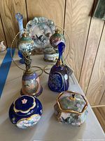Photo showing several Fenton glass collectibles including decorative hand-painted bells, blue trinket boxes, and a blue vase arranged on a table.
