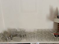 Wide view of the Fostoria American pattern collection showing multiple glasses, plates, and trays arranged on a surface.