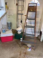 Photo of wooden duck sculpture on green box next to ladder, cooler, metal bucket and paint cans.