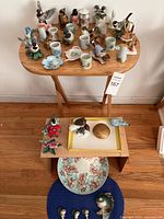 Overview of Lenox porcelain bird figurines, small vases, several decorative plates, and additional items on a folding wooden table and an adjacent cardboard box, showing the variety included in the lot.