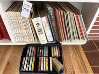 Image of a white shelving unit with vinyl records, two cookbooks, and cassette tapes below them in a tray.