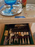 Close-up photo of silver plate forks, spoons, and utensils arranged inside the green lined flatware box.