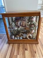 Full view of a small oak wood and glass display cabinet on wood floor, showing the front glass panel with shelves and various figurines inside.