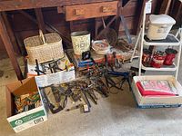 Tools and various items piled on floor including hand tools, wires, wicker basket, rolls of wire, vintage Olgers tins
