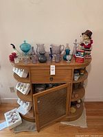 Overview photo of sideboard with assorted colored vintage glassware, porcelain pipe, collectibles, and vintage toy figure
