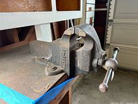 Side view of vintage cast iron bench vise mounted on workbench showing brand and number markings.