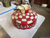 Side view of entire glass shade showing red and white checker pattern and “Shakey’s” lettering