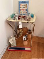 Vintage toothpick holders and related items displayed on a cream-colored TV tray with gold metal legs, alongside other decorative items and boxed candles on floor.
