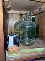 Three large glass water carafes, two clear and one green, and a decorative milk holder shaped like a small house attached to a black and white container.