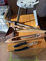 Photo showing antique axe, two blade sharpeners, wooden spindle tool, metal pliers on a wooden surface.