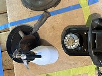 Photo showing the whip cream dispenser, hand crank drill, and antique phone together on a beige surface with blue and yellow tape.