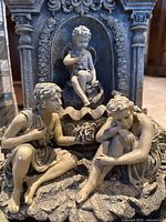 Close-up of the two seated angelic figures and smaller figure above, detailed with floral elements and ornate textured base.