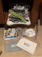 Photo of the Nintendo Wii console, balance board, cables, 2 Wii controllers with silicone protectors, 2 games, and 2 Wii operation manuals.