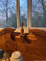 Close-up of the top center detailing and finial of the headboard showing wood grain and carved features