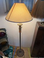 Antique upright lamp with beige fabric shade, wooden and metal base standing on floor.