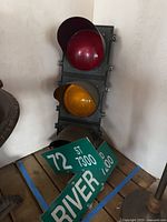 Traffic light with red and amber lenses against wall with two green street signs lying at its base