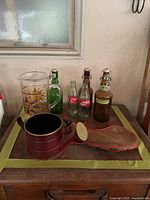 Full view of all items together on table showing watering can, suede flask, vintage Coke and beer bottles, and sun water jug
