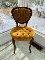 Front view of the gold velvet tufted accent chair showing the detailed tufting on the seat and backrest along with curved wooden legs.